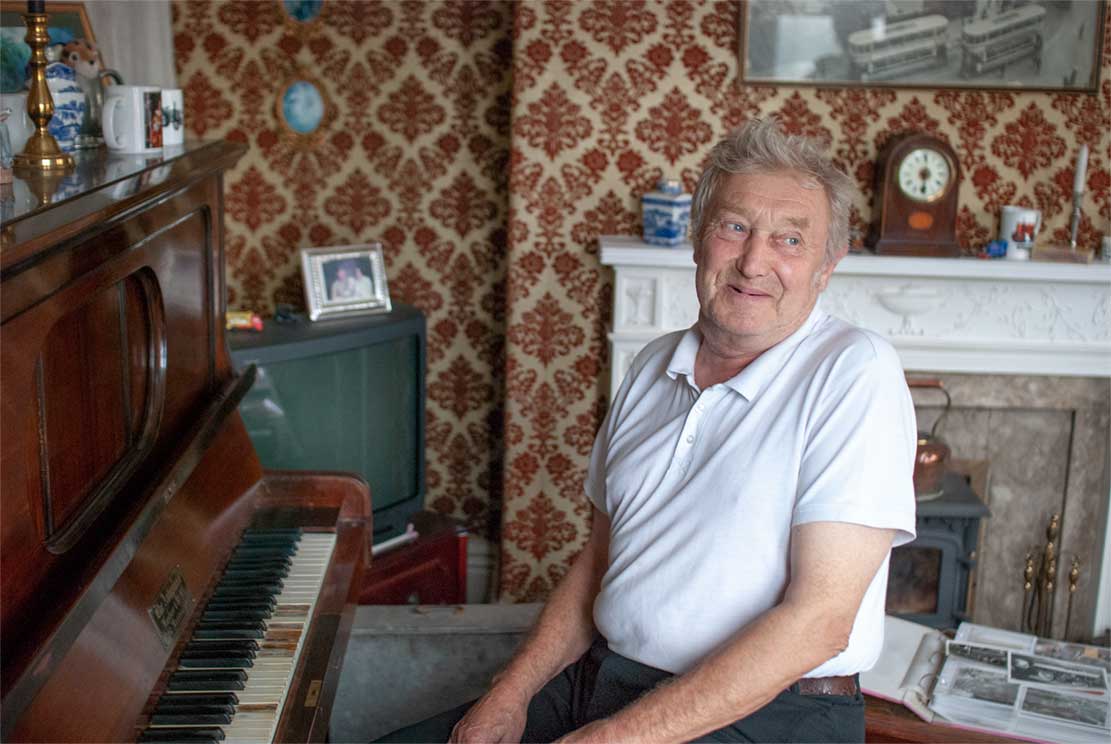 John (69), like Jozef's father, sitting behind a piano turned towards you smiling.